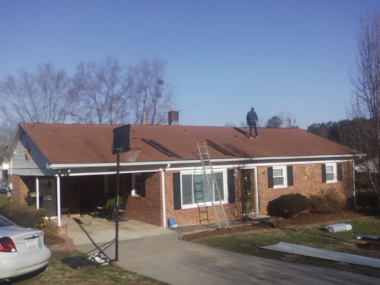 Roofer stripping a shingle roof on a brick ranch before metal panels in Holbrook
