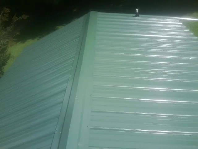 New green metal panels meeting at the ridge of a roof — Flat Roof Repair work by our crew in Holbrook