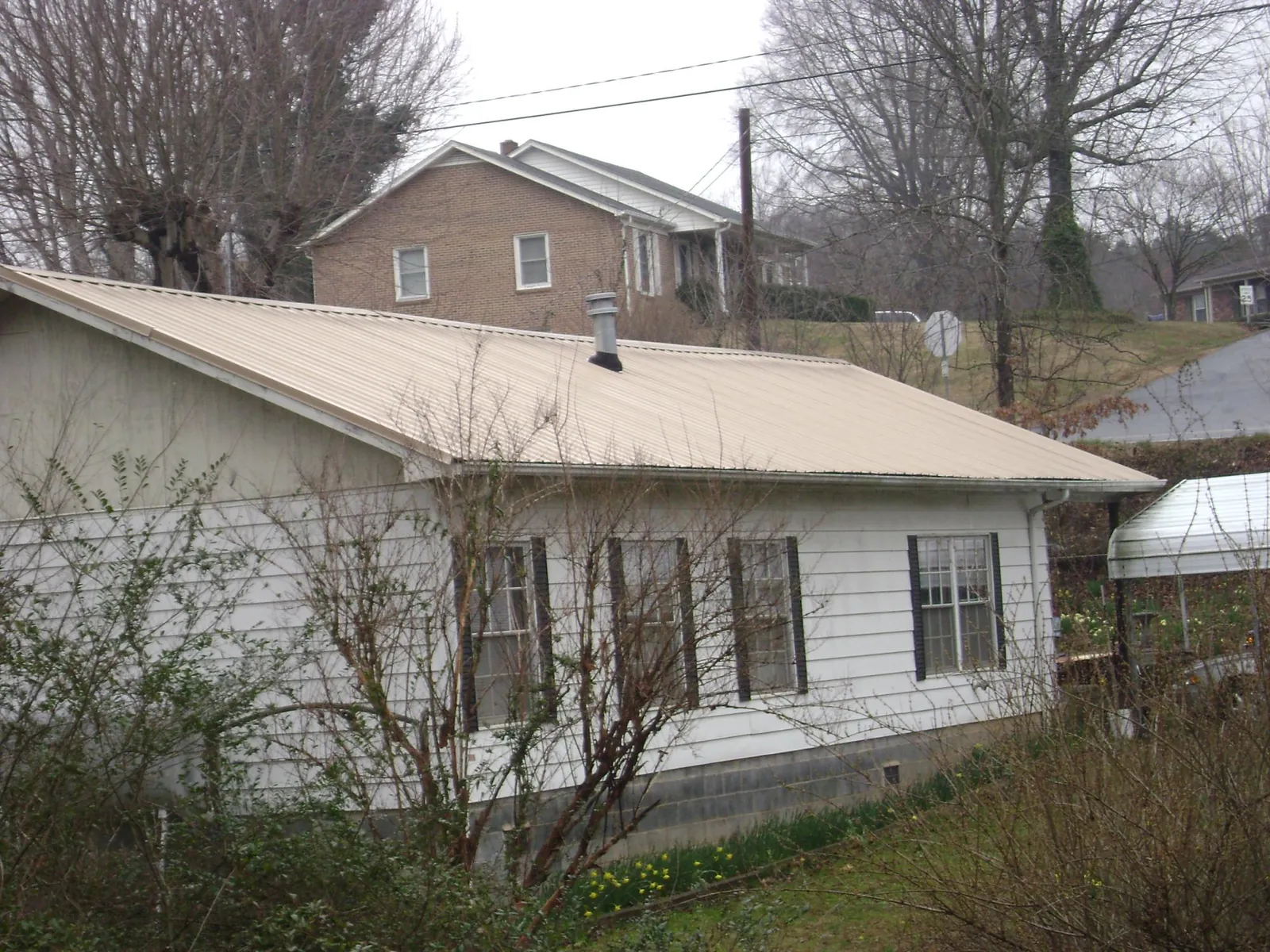 Tan metal roof on a white sided house set into a hillside — Commercial Roofing by Roofing Brothers in Holbrook